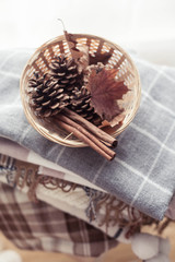 Plaids. Autumn cozy interior. On a wooden chair is a stack of warm blankets. Candles, leaves, cones, basket, cinnamon. Autumn. Winter.