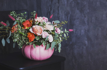Autumn floral bouquet in colored pumpkin vase on black chair, copy space