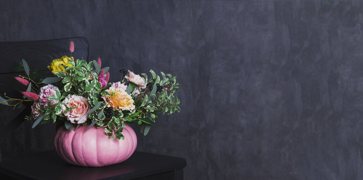 Autumn floral bouquet in colored pumpkin vase on black chair, banner