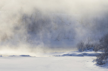 Fog over the river on a frosty morning and white snowy field in winter
