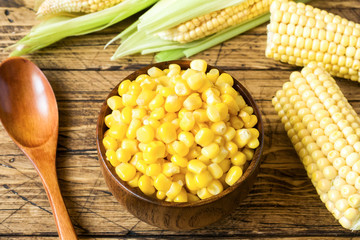 Canned corn in a wooden plate and cob of fresh corn on a rustic wooden background
