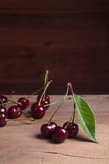 Red sweet cherry with green leaf on wooden background.