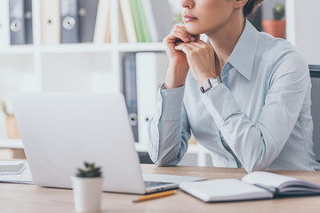 cropped shot of thoughtful adult businesswoman sitting at workplace