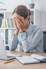 Naklejka premium stressed adult businesswoman covering face with hands at workplace
