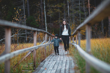 boy with his mother on a walk in the woods go on a wooden walkway