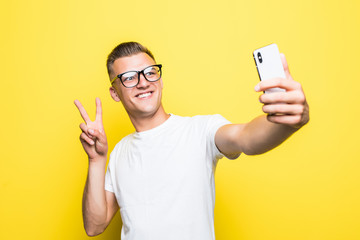 Cheerful man looking at camera and taking selfie on yellow background
