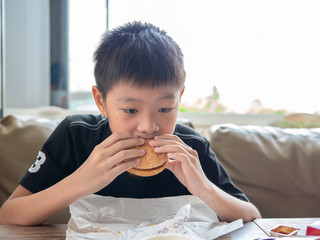 A sad moody boy eating hamburger in the hamburger shop