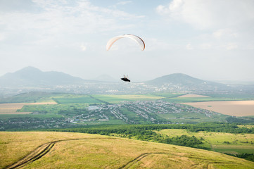 A white-orange paraglider flies over the mountainous terrain