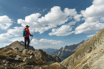 Fototapeta na wymiar A bearded man in sunglasses and a cap with a backpack stands on top of a rock and looks into a rocky valley high in the mountains. The concept of tourism and easy trekking in the mountains outdoor