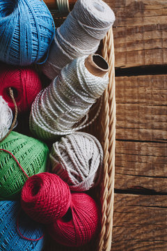 Needlework, macrame, knitting. Yarn and threads of bright colors in a wicker basket on a wooden background. Women's hobby.