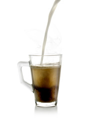 Un chorro de leche cayendo sobre una taza de cristal rellena de té