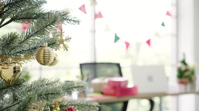 Happy Asian woman holding xmas ornament for decorate christmas tree in her office. Attractive female and her friends spend holiday celebration. Winter holidays concept.