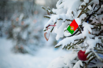 Portugal flag. Christmas background outdoor. Christmas tree covered with snow and decorations and Portuguese flag.  Feliz ano novo / Navidad/ New Year / Christmas holiday greeting card.