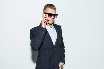 Confident businessman in black suit and sunglasses talking on mobile phone, isolated on white background