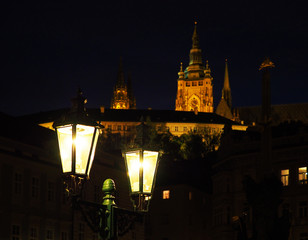 Fototapeta na wymiar Night Prague, Czech Republic. Antique foreground lantern, illuminated, Prague Castle, Holy Trinity Column, God’s eye placed on top. Lesser Town Square