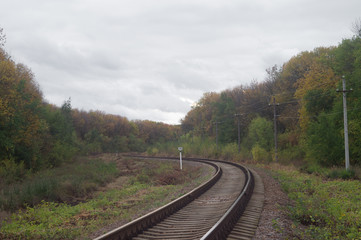 Fototapeta na wymiar Autumn railway lines stretching beyond the horizon. Overcast October industrial landscape under heavy leaden sky