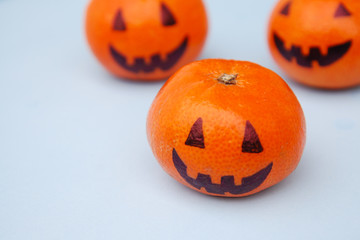 Funny orange mandarins or tangerines pumpkin painted in the form of icons of Halloween on the light backround