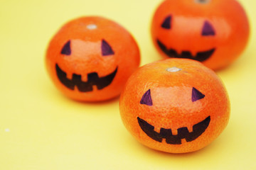 Funny orange mandarins or tangerines pumpkin painted in the form of icons of Halloween on the yellow backround