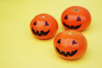 Funny orange mandarins or tangerines pumpkin painted in the form of icons of Halloween on the yellow backround