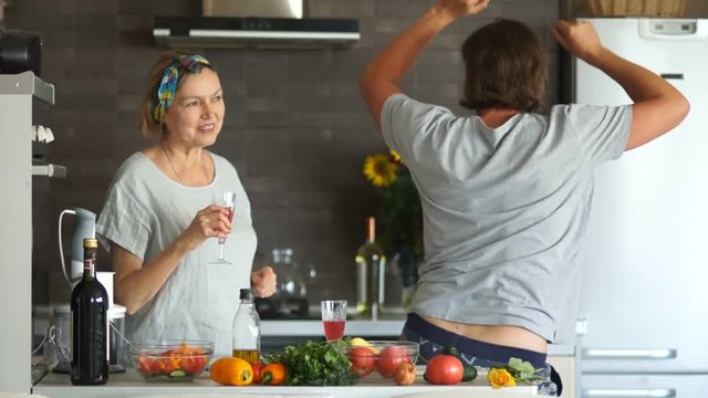 Mature woman and young man. A couple with an age difference prepare the salad in the kitchen, they relax to the music and drink wine from the glasses