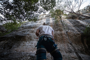 From below of anonymous man in harness looking up at mountain and checking partner climbing cliff  