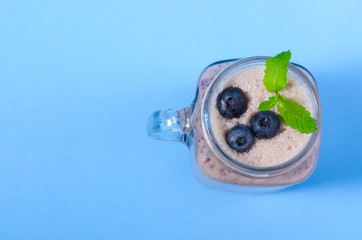 Blueberry smoothie with mint in mason jar glass with berries and mint. Above view on blue table. Healthy food.
