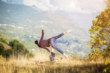 Giovane coppia pratica acroyoga e yoga all'aperto in montagna al parco
