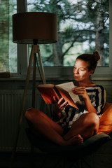 Young woman reading a book at home by the window