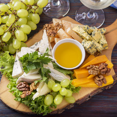 Cheese plate served with white wine, grape and nuts. Assorted cheeses on wooden board. Closeup. Top view.