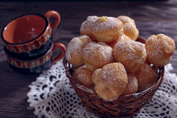 Fresh handmade profiteroles in a wicker basket on a lace doily next to two coffee cups to drink coffee