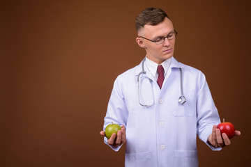 Young man doctor wearing eyeglasses against brown background