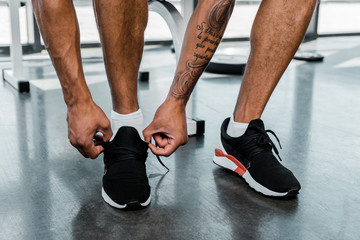 cropped shot of young sportsman tying shoelaces in gym