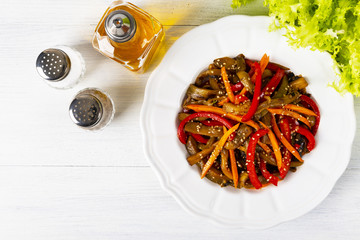Vegetable salad. Aubergines fried, pepper, carrots on a white plate. The concept of healthy eating. White wooden background. Top view. Copy space