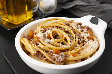 Pasta with bolognese sauce. Parmesan and olive oil. In a white frying pan. The background is black. Italian food.