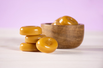 Lot of whole caramel cream candy butterscotch variety with wooden bowl with pastel pink in background