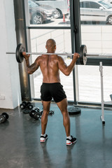 back view of athletic young shirtless man lifting barbell in gym