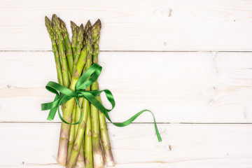 Bundle of lot of whole fresh green asparagus spear tied by green ribbon flatlay on white wood