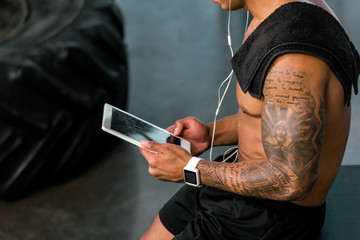 cropped shot of muscular tattooed sportsman using digital tablet in gym
