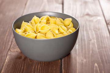 Lot of whole raw yellow pasta conchiglie variety in a grey ceramic bowl on brown wood