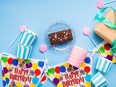 Happy Birthday party items flat lay. Candles, gift box, decoration banner, paper glasses, chocolate cake