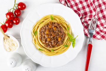 Pasta with Bolognese sauce. In a white plate. Parmesan cheese, a branch of tomatoes and a fork. The background is white. Italian food. Copy space. Top view. Horizontal shot.