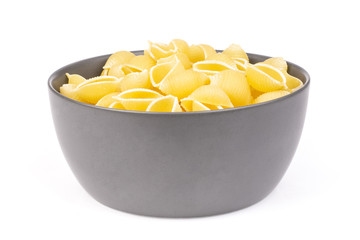 Lot of whole raw yellow pasta conchiglie variety in a grey ceramic bowl isolated on white background