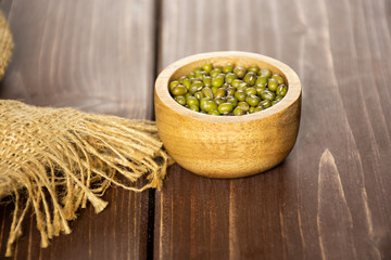 Lot of whole dry green mung beans with a piece of jute cloth with wooden bowl on brown wood