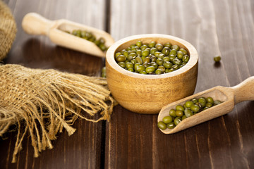 Lot of whole dry green mung beans in two scoops with wooden bowl on brown wood