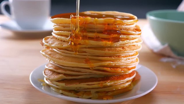 Melted golden honey is doused on just cooked pancakes on table, ready to be eaten