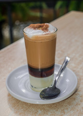 Coffee with milk, liqueur and cinnamon on white dish with spoon