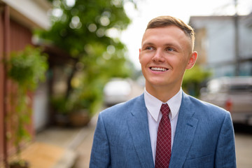 Portrait of happy young businessman thinking in the streets outdoors