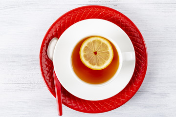 Tea with lemon in a white mug on a red plate. On a wooden table. Tea spoon. Top view.
