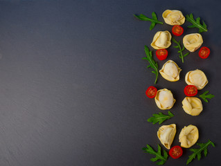 Frozen tortellini on the black background. Italian tortellini with fresh ricotta leaves and tomatoes on a black stone board. Top view.