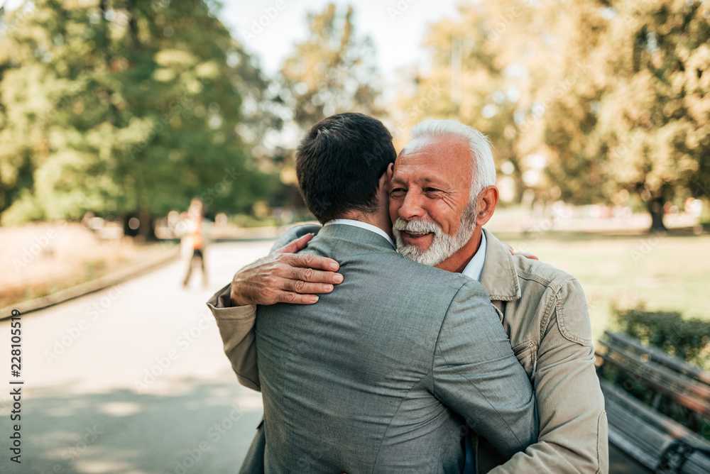 Wall mural Elderly father and adult son hugging in the park.